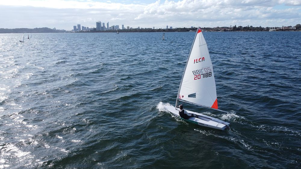 A small sailing boat on the Swan River with the Perth skyline behind